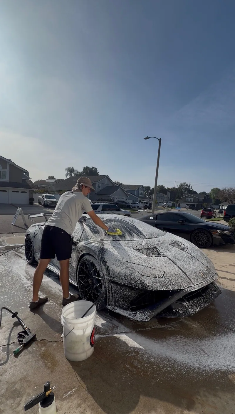Carefully hand-washing a foam-covered sports car in a driveway