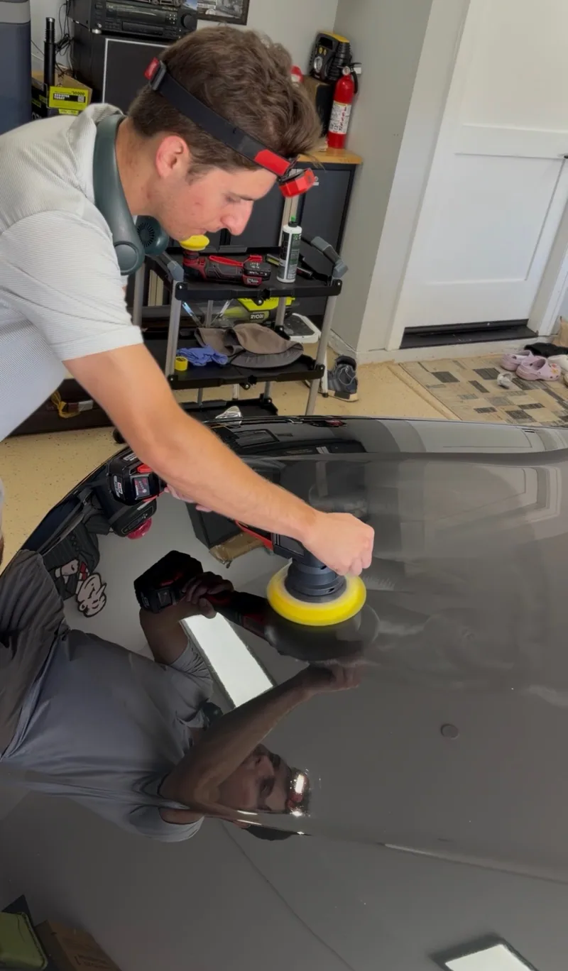 Using a yellow-pad polisher on a black hood, with my reflection visible in the paint